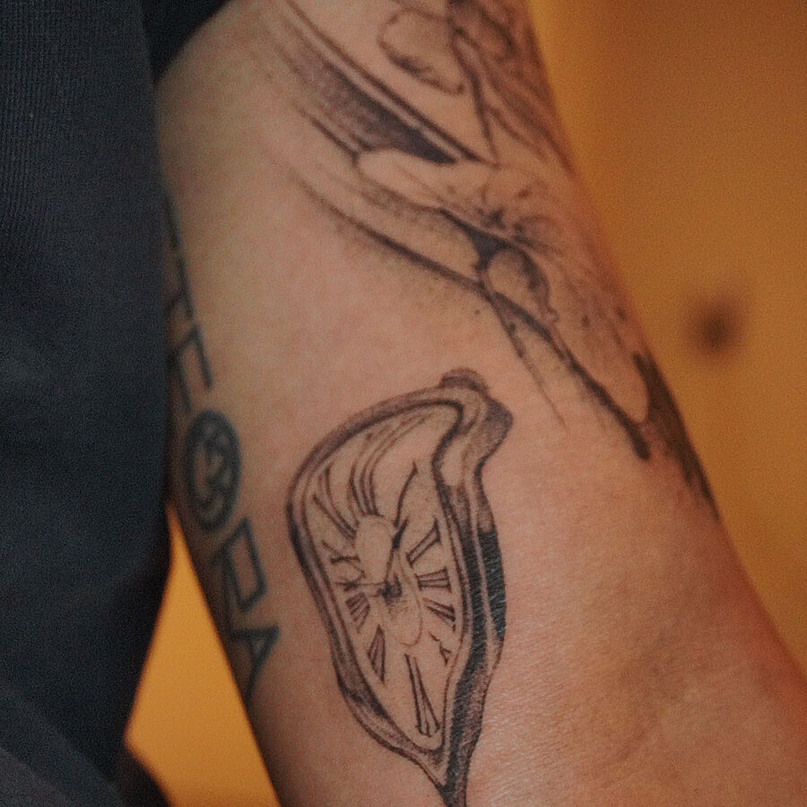 Close-up of a fine-line melting clock tattoo on a forearm